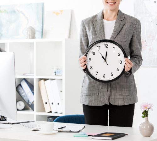 cropped image of attractive businesswoman holding wall clock in office